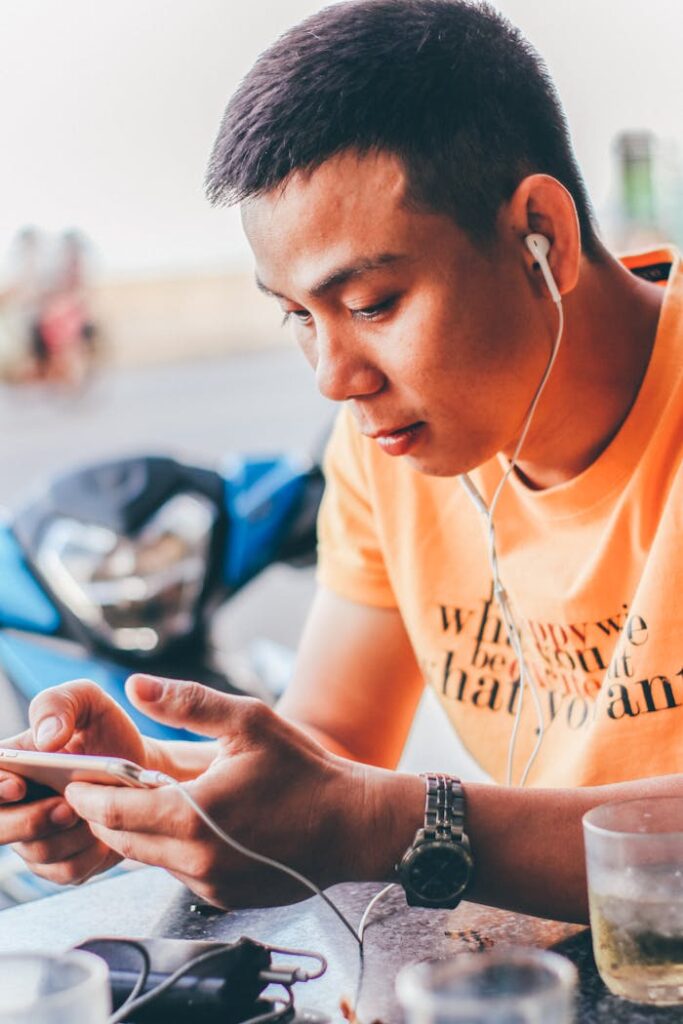 Casual outdoor scene of a young man focused on mobile gaming with earphones on.