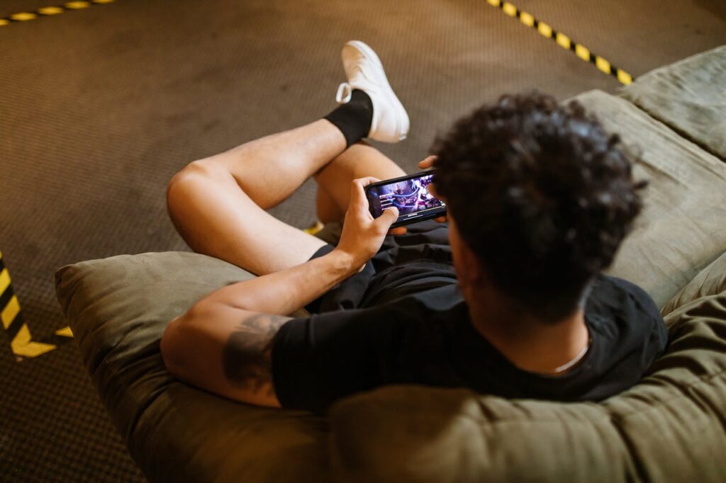 pexels-photo-7915284 A man relaxing on a sofa playing a video game on his smartphone.