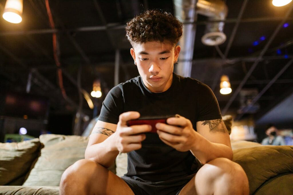 pexels-photo-7915294 Focused young man engaged in gaming on smartphone indoors, enjoying online recreation.